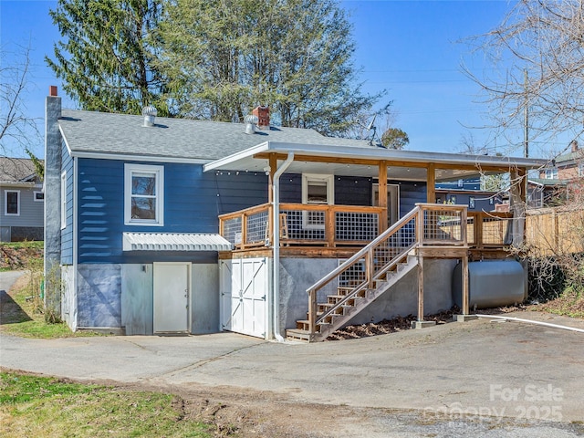 view of front of home featuring heating fuel, stairway, a chimney, and a shingled roof