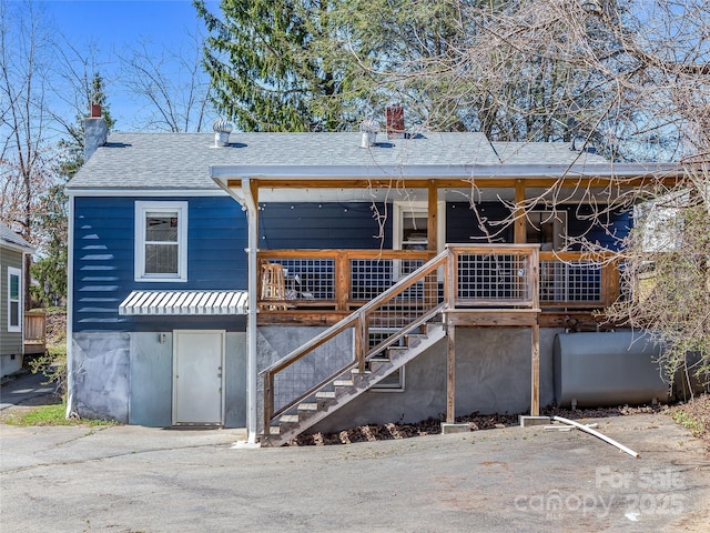 view of front of home with stairway, heating fuel, a porch, and roof with shingles