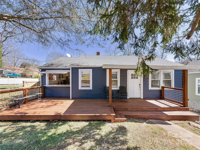 rear view of property with a wooden deck, fence, and a shingled roof