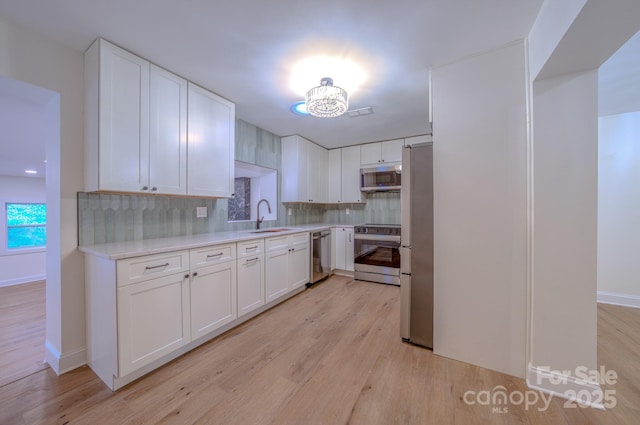 kitchen with stainless steel appliances, a sink, light wood-style floors, light countertops, and decorative backsplash