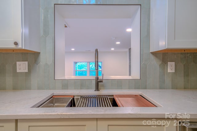 kitchen featuring light stone counters, recessed lighting, decorative backsplash, white cabinets, and a sink