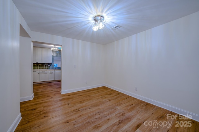 empty room with light wood-style floors, baseboards, visible vents, and a chandelier