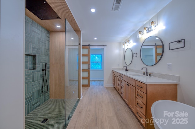 full bathroom featuring double vanity, wood finished floors, a tile shower, a freestanding tub, and a sink