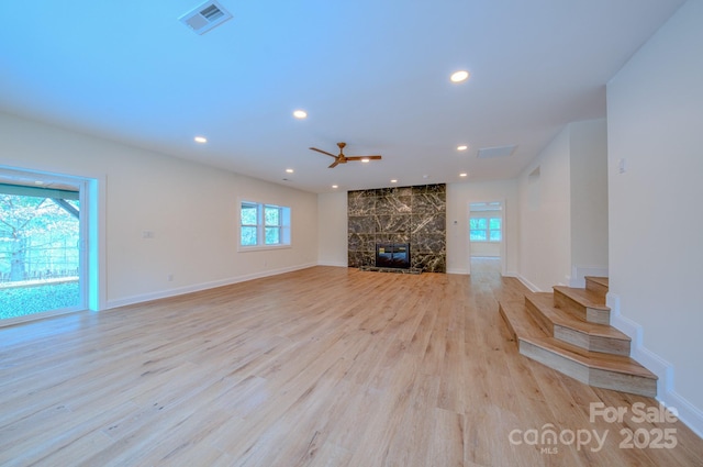 unfurnished living room with a wealth of natural light, a high end fireplace, visible vents, and light wood-style flooring