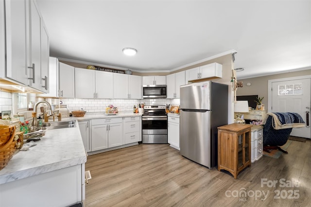 kitchen with crown molding, light countertops, backsplash, appliances with stainless steel finishes, and a sink