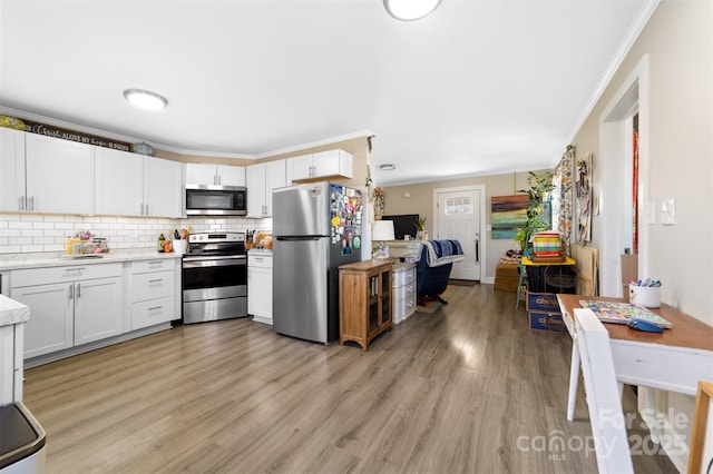 kitchen with light countertops, light wood-style flooring, decorative backsplash, appliances with stainless steel finishes, and ornamental molding