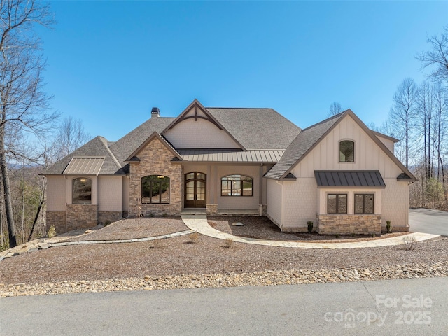 view of front facade with a standing seam roof, stone siding, french doors, a shingled roof, and metal roof