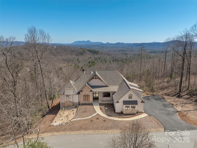 view of front of house with a wooded view, a shingled roof, board and batten siding, stone siding, and a mountain view