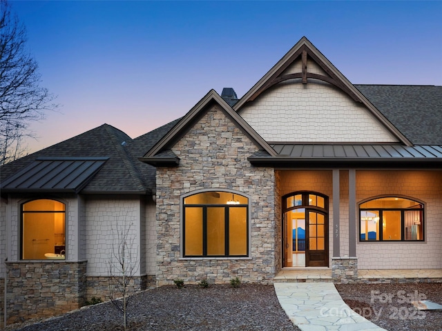 view of front of house featuring a standing seam roof, stone siding, roof with shingles, and metal roof