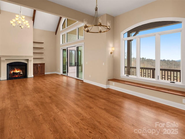 unfurnished living room with a wealth of natural light, wood finished floors, and a chandelier