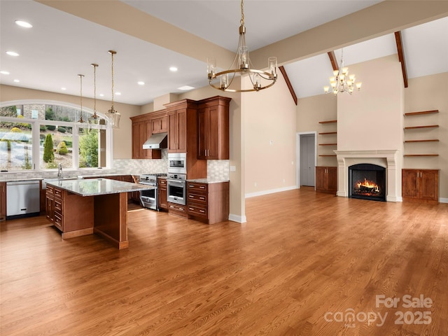 kitchen featuring under cabinet range hood, a sink, appliances with stainless steel finishes, light wood finished floors, and a chandelier