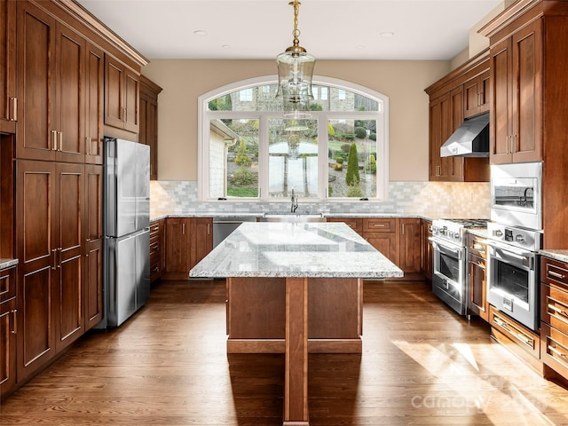 kitchen with a kitchen island, dark wood-style flooring, under cabinet range hood, appliances with stainless steel finishes, and backsplash