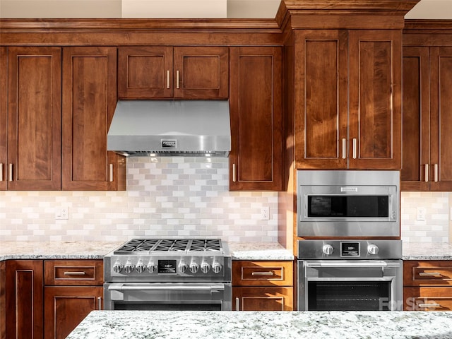 kitchen featuring light stone counters, decorative backsplash, appliances with stainless steel finishes, and wall chimney range hood