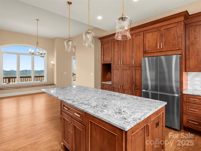 kitchen with brown cabinetry, light wood-type flooring, stainless steel fridge, and decorative backsplash