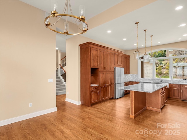 kitchen with brown cabinetry, freestanding refrigerator, light wood-style floors, a notable chandelier, and tasteful backsplash