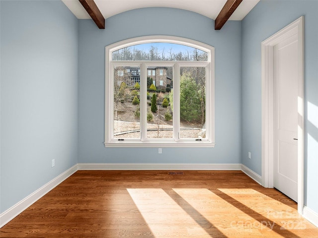 spare room with beamed ceiling, baseboards, and wood finished floors