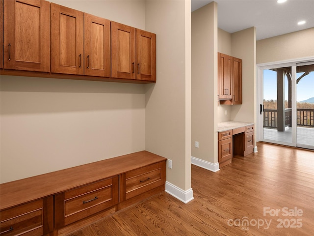 mudroom featuring recessed lighting, baseboards, built in desk, and light wood finished floors