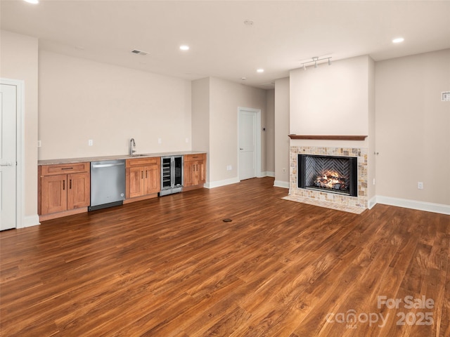 unfurnished living room with dark wood finished floors, a sink, indoor wet bar, wine cooler, and a tiled fireplace