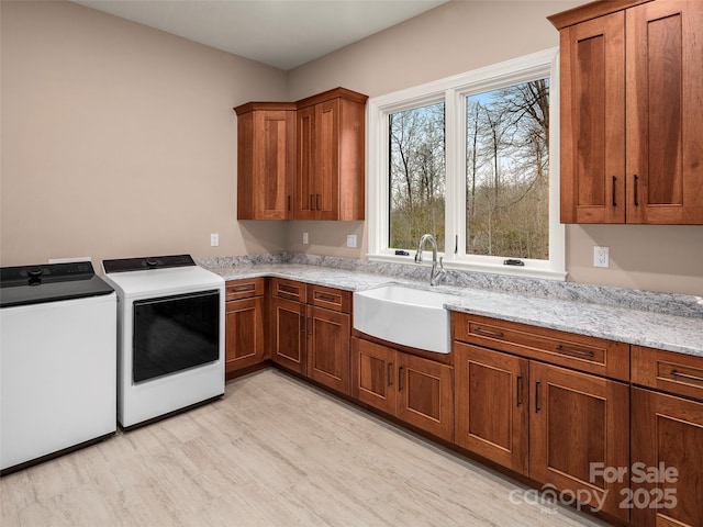 laundry room with washer and clothes dryer, cabinet space, light wood-style flooring, and a sink