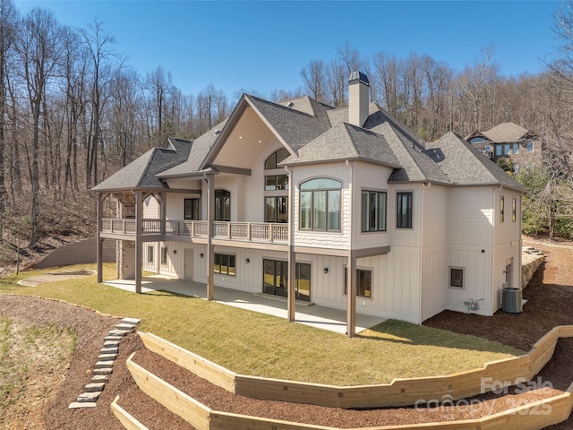 back of property with a patio, cooling unit, roof with shingles, a yard, and a chimney