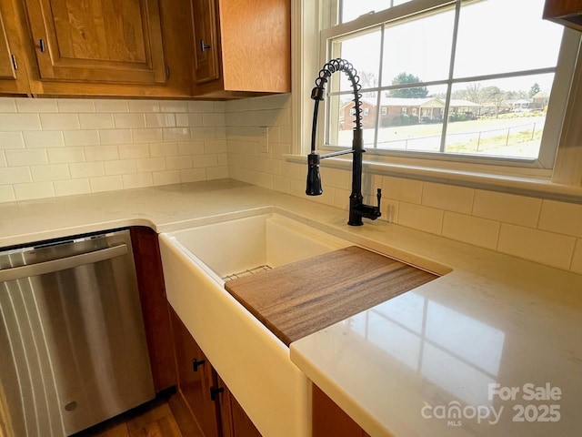 kitchen featuring decorative backsplash, dishwasher, brown cabinetry, and light countertops