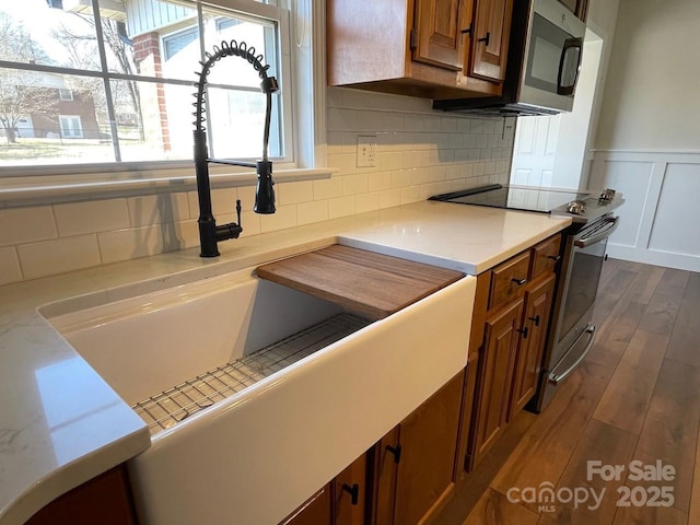 kitchen with dark wood-style floors, brown cabinets, appliances with stainless steel finishes, and wainscoting