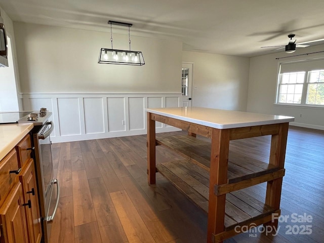 dining space with a wainscoted wall, dark wood-type flooring, a ceiling fan, and a decorative wall