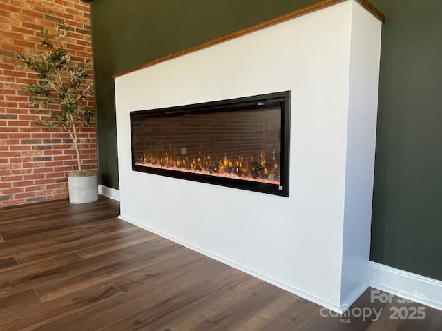 interior details featuring wood finished floors, baseboards, and a warm lit fireplace