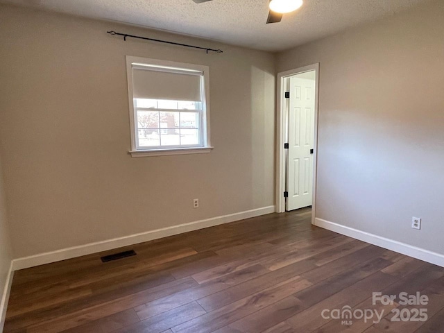 spare room featuring visible vents, dark wood-type flooring, baseboards, a textured ceiling, and a ceiling fan