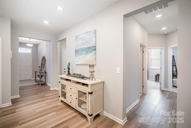 hall featuring light wood-type flooring, visible vents, and baseboards