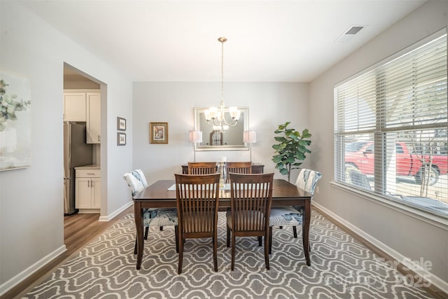 dining space featuring a chandelier, visible vents, baseboards, and wood finished floors