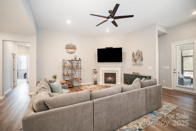 living room with a ceiling fan, wood finished floors, baseboards, a fireplace with flush hearth, and recessed lighting