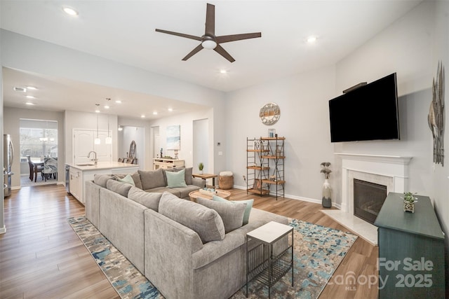 living area featuring light wood finished floors, baseboards, a fireplace with flush hearth, recessed lighting, and a ceiling fan