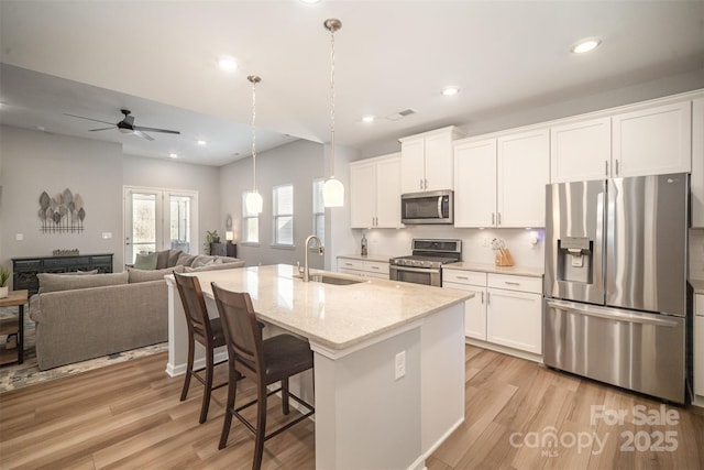 kitchen with a sink, open floor plan, white cabinetry, stainless steel appliances, and light wood finished floors