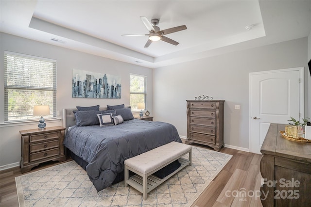 bedroom featuring visible vents, baseboards, ceiling fan, a raised ceiling, and light wood-type flooring