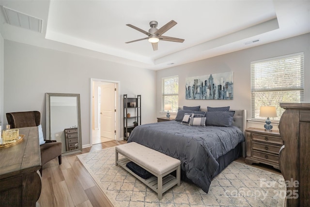 bedroom with a tray ceiling, visible vents, and light wood finished floors