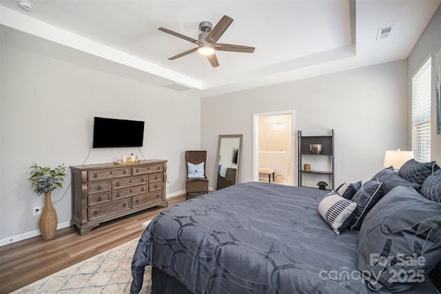 bedroom featuring visible vents, a tray ceiling, wood finished floors, baseboards, and ceiling fan