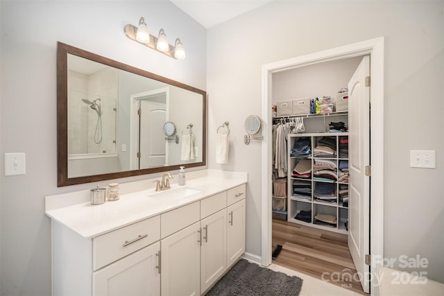 bathroom with a walk in closet, wood finished floors, vanity, and walk in shower