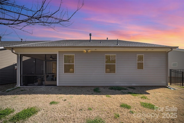 back of property at dusk featuring a lawn, fence, a sunroom, and a shingled roof