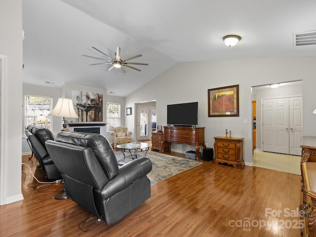 living room featuring light wood-type flooring, lofted ceiling, visible vents, and ceiling fan