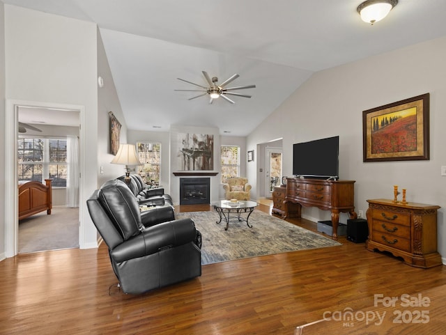 living room with a glass covered fireplace, high vaulted ceiling, wood finished floors, and a ceiling fan