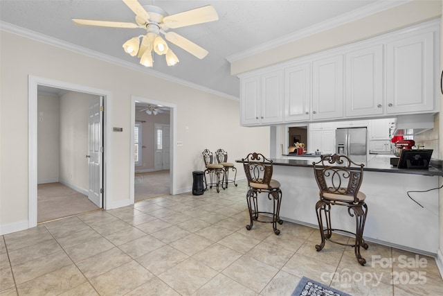 kitchen with dark countertops, crown molding, stainless steel refrigerator with ice dispenser, and ceiling fan