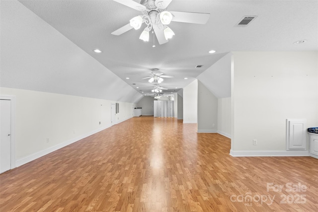 additional living space featuring light wood finished floors, visible vents, a ceiling fan, vaulted ceiling, and baseboards