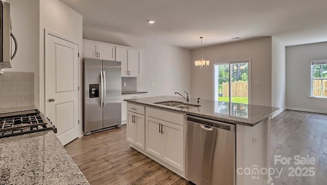 kitchen with stone countertops, decorative backsplash, appliances with stainless steel finishes, wood finished floors, and a sink