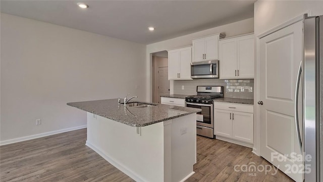 kitchen with a center island with sink, stainless steel appliances, tasteful backsplash, white cabinets, and a sink