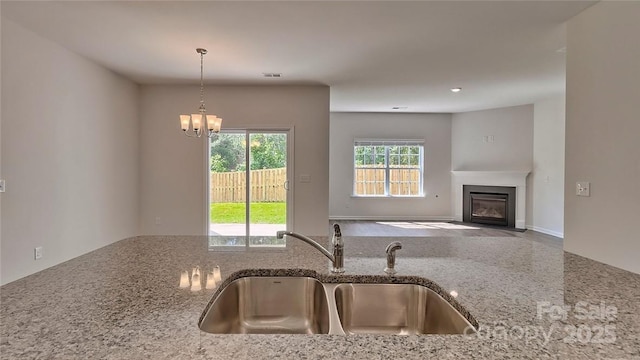 kitchen with a fireplace with flush hearth, light stone counters, an inviting chandelier, pendant lighting, and a sink