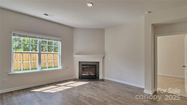 unfurnished living room with a fireplace with flush hearth, wood finished floors, visible vents, and baseboards