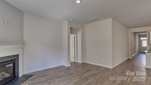 unfurnished living room featuring baseboards, wood finished floors, and a glass covered fireplace