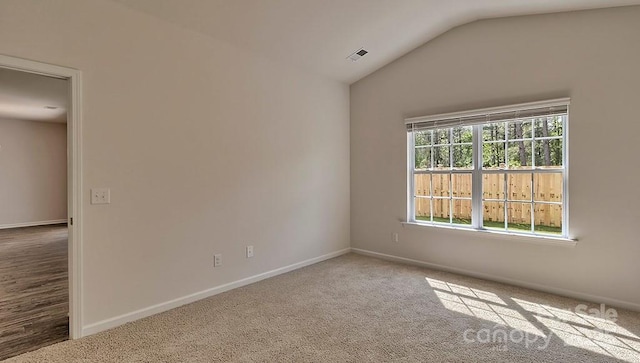 carpeted spare room with lofted ceiling, baseboards, and visible vents