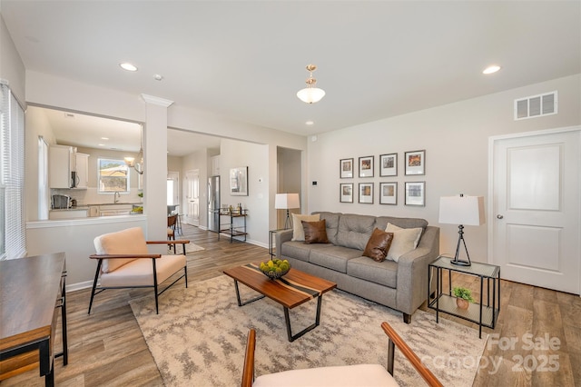 living room with visible vents, baseboards, light wood-type flooring, recessed lighting, and ornate columns